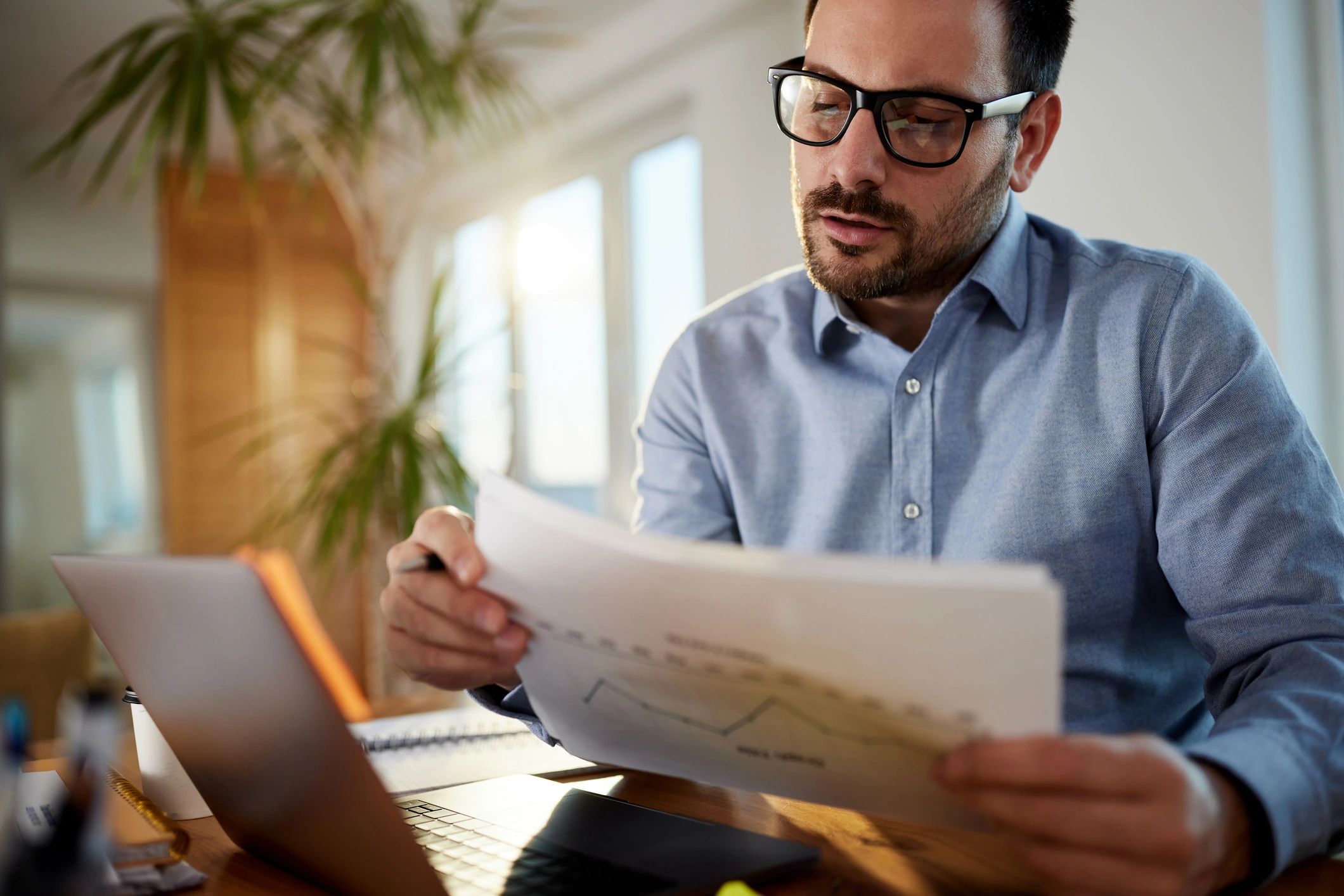Investor working on laptop and reviewing reports in a home office